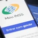Celular com a tela do aplicativo Meu INSS aberta ao lado de cartão da Previdência Social sobre teclado de notebook