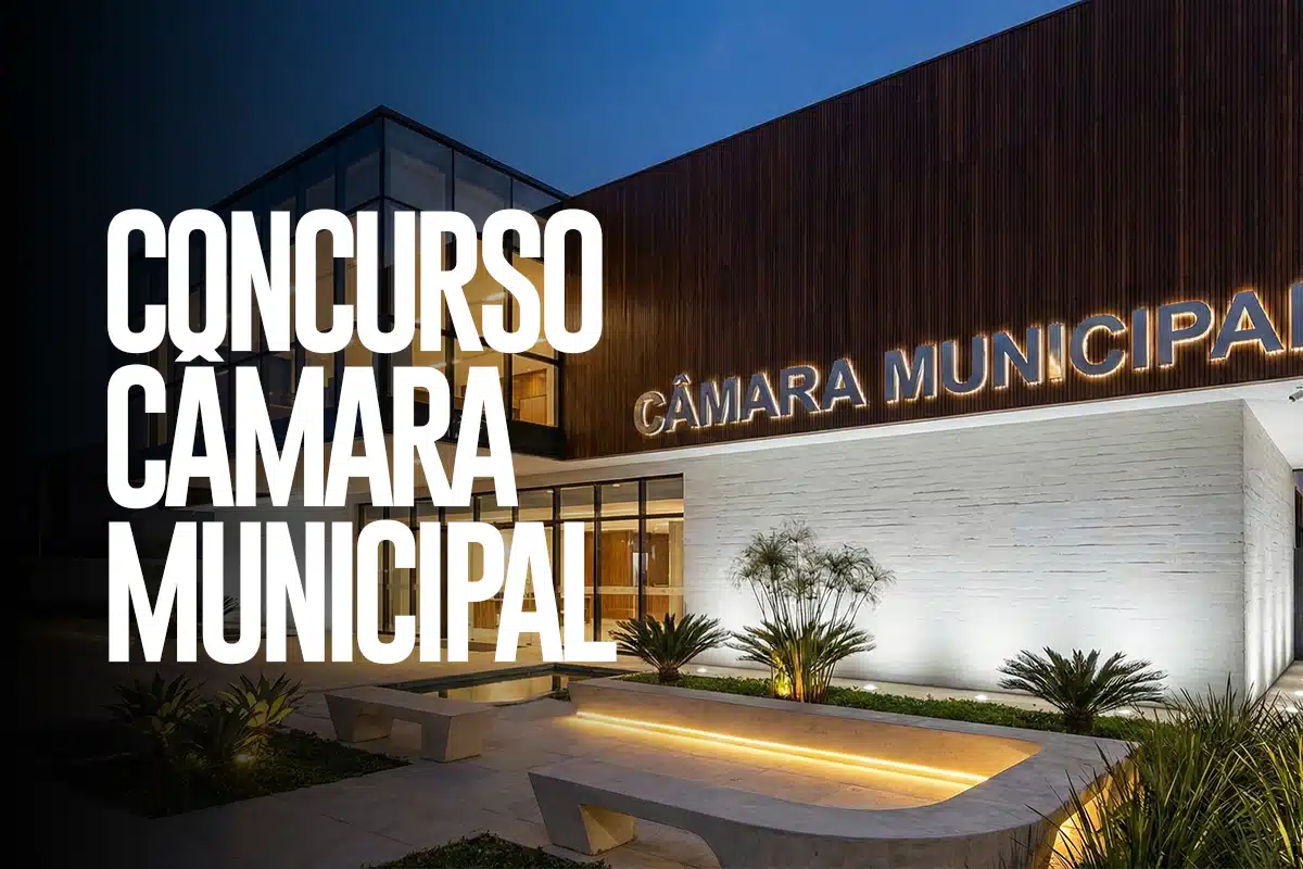 Vista noturna da fachada iluminada da Câmara Municipal com letreiro retroiluminado, jardim ornamental e bancos de concreto na entrada