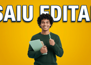 Jovem negro sorridente, cabelo crespo, suéter verde, segura cadernos e caneta em fundo amarelo com texto "Saiu Edital"