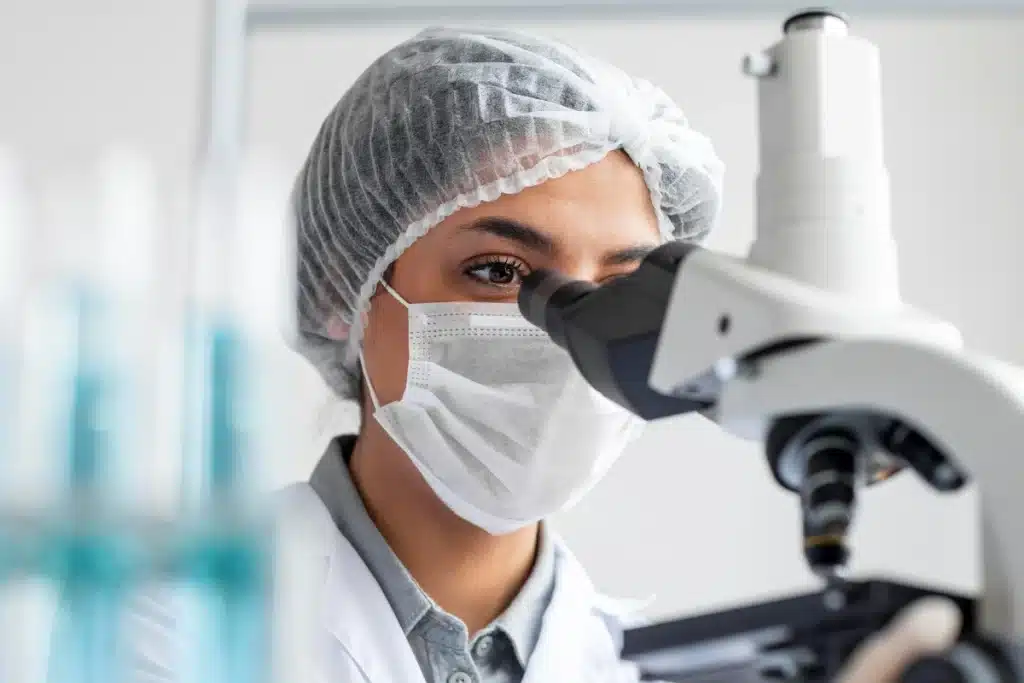 Biomédica usando microscópio em laboratório durante análise científica, representando cursos em áreas de alta demanda.