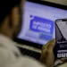 Homem acessa serviços da Receita Federal pelo celular enquanto visualiza portal do Imposto de Renda no notebook