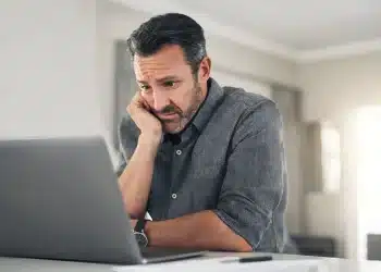 Homem preocupado olhando para o laptop em casa, lidando com o estresse, representando os desafios de carreira após os 40 anos.