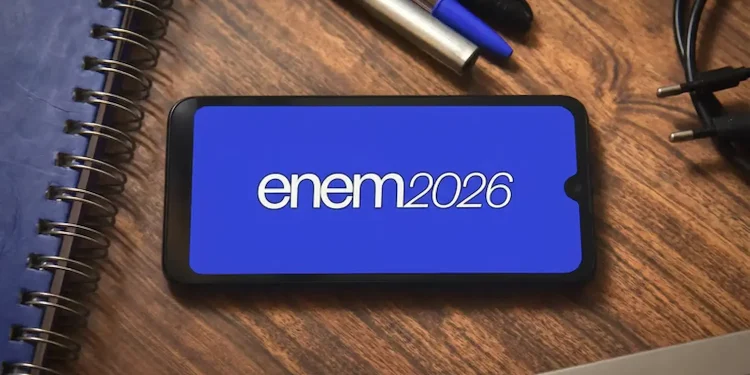 Tela de smartphone com o logo do Enem 2026 em fundo azul, com canetas e cadernos ao redor.