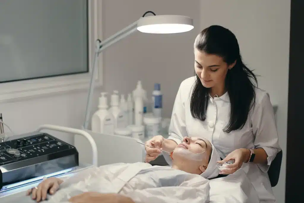 Esteticista aplicando produto facial em paciente durante tratamento de cuidado e manutenção da pele.