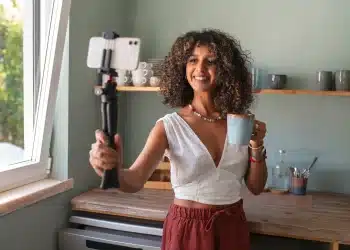 Influenciadora sorrindo enquanto tira uma selfie com um copo de café, representando a rotina e estilo de vida dos influenciadores digitais no Brasil.