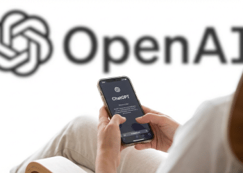 Pessoa segurando iPhone com tela de boas-vindas do ChatGPT, logo da OpenAI ao fundo em parede branca