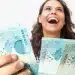 Pessoa sorrindo e segurando cédulas de 100 reais, ilustrando tema sobre datas de pagamento do salário em abril.