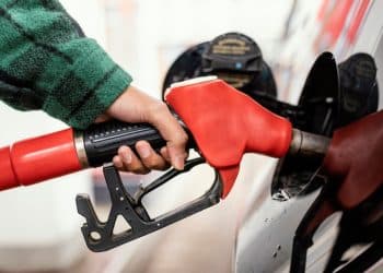 Pessoa abastecendo gasolina em um posto de combustíveis com bomba vermelha, com o veículo visível ao fundo.