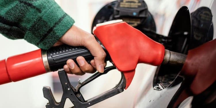 Pessoa abastecendo gasolina em um posto de combustíveis com bomba vermelha, com o veículo visível ao fundo.