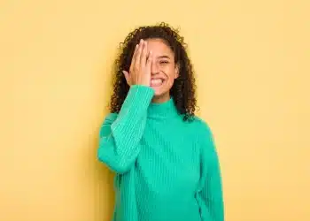 Mulher sorrindo e cobrindo parcialmente o rosto com a mão, representando dualidade de personalidade, tema de psicologia sobre timidez e extroversão.