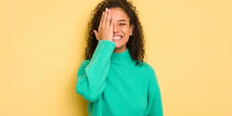 Mulher sorrindo e cobrindo parcialmente o rosto com a mão, representando dualidade de personalidade, tema de psicologia sobre timidez e extroversão.