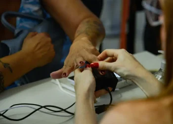 Atendente realiza coleta de biometria das digitais de cidadão em posto de atendimento, ilustrando o cadastro biométrico exigido para programas sociais até dezembro de 2026