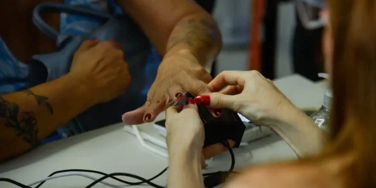 Atendente realiza coleta de biometria das digitais de cidadão em posto de atendimento, ilustrando o cadastro biométrico exigido para programas sociais até dezembro de 2026
