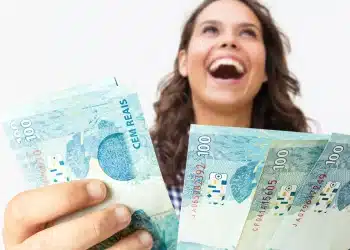Pessoa sorrindo segurando notas de cem reais, representando oportunidades de profissões bem pagas sem necessidade de faculdade.