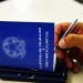 Mão segurando caneta sobre carteiras de trabalho azuis em ilustração sobre as mudanças propostas na CLT para o direito à desconexão do trabalhador