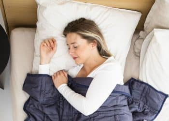 Mulher dormindo tranquilamente em cama com travesseiros brancos e cobertor azul, representando a qualidade do sono e seus estágios de descanso