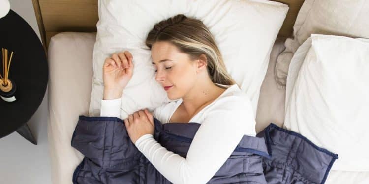 Mulher dormindo tranquilamente em cama com travesseiros brancos e cobertor azul, representando a qualidade do sono e seus estágios de descanso