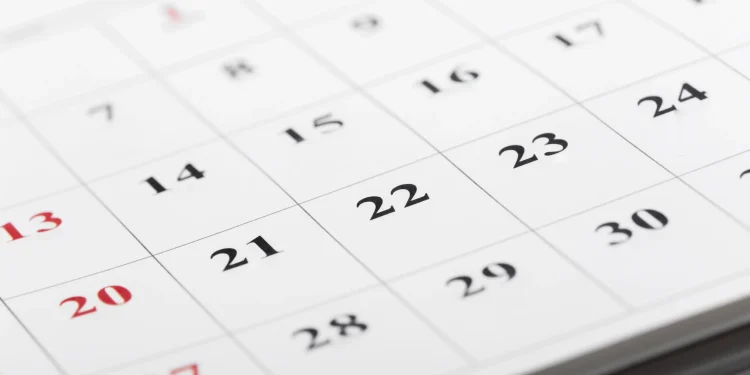Calendário de parede em close com datas em preto e vermelho, sendo os números em vermelho indicando domingos e feriados, representando o calendário da Semana Santa 2026 e a dúvida sobre a Quinta-feira Santa ser ou não feriado nacional no Brasil