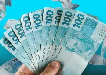 Mão segurando várias notas de 100 reais em leque representando o reajuste do salário mínimo em 2027 para aposentados e pensionistas do INSS