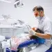 Dentista realizando procedimento odontológico em paciente mulher em consultório