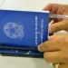 Mãos segurando a Carteira de Trabalho e Previdência Social com uma caneta, representando o processo de solicitação do seguro-desemprego em 2026