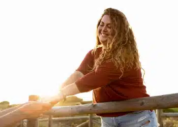 Mulher sorrindo ao ar livre durante um momento tranquilo de solitude e bem-estar emocional.