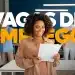 Mulher negra sorridente com cabelo cacheado segura documentos em escritório moderno com texto “Vagas de Emprego”.
