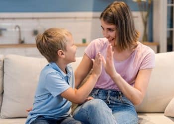 Mãe e filho brincam de bater palmas no sofá de casa.
