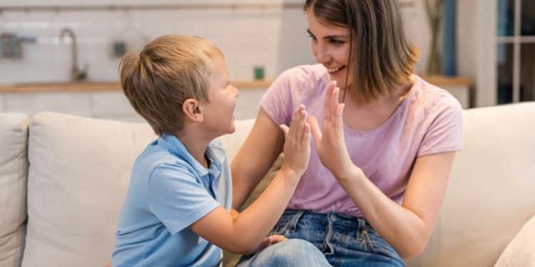 Mãe e filho brincam de bater palmas no sofá de casa.
