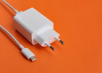 Carregador USB-C branco com cabo sobre fundo laranja vibrante.