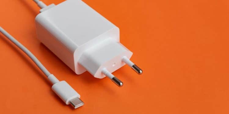 Carregador USB-C branco com cabo sobre fundo laranja vibrante.