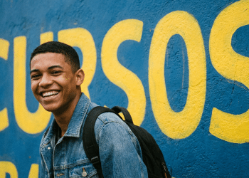 Jovem estudante sorridente em frente a muro com a palavra Cursos.