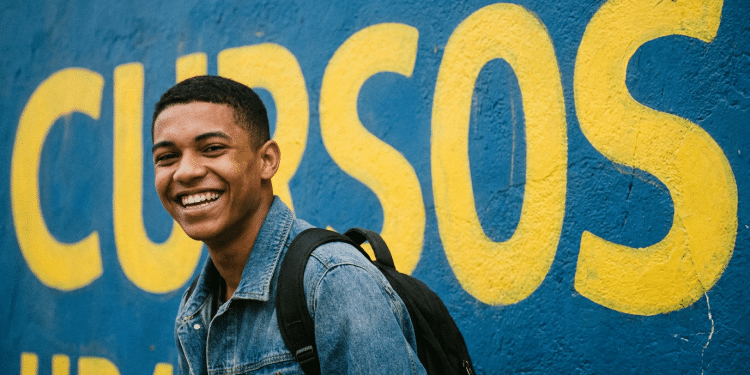 Jovem estudante sorridente em frente a muro com a palavra Cursos.