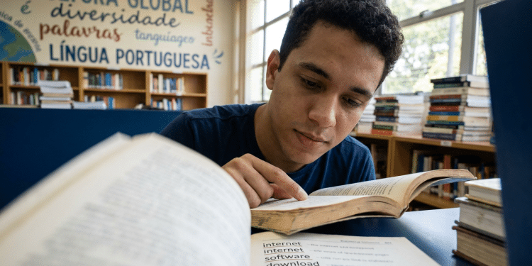 Jovem estuda língua portuguesa em biblioteca escolar.