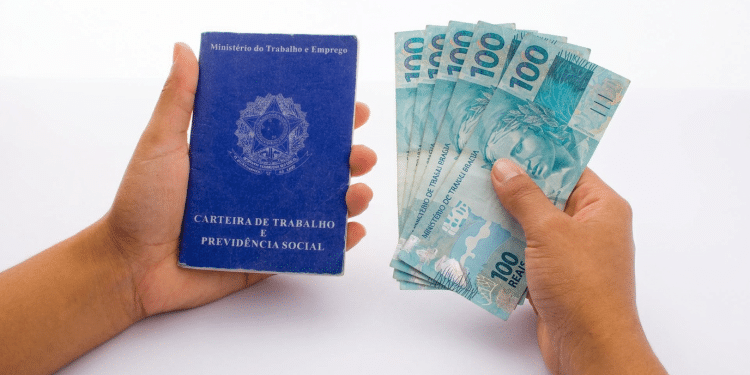 Mãos segurando carteira de trabalho e notas de 100 reais.