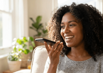 Mulher sorridente usa comando de voz no celular em casa.