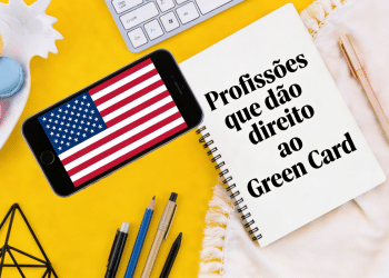 Caderno com a frase "Profissões que dão direito ao Green Card" e celular exibindo a bandeira dos EUA.