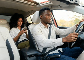 Mulher usando smartphone no banco do passageiro e homem dirigindo o carro.