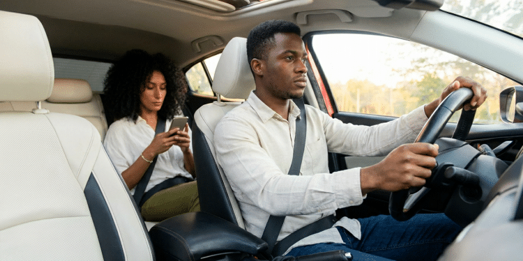 Mulher usando smartphone no banco do passageiro e homem dirigindo o carro.