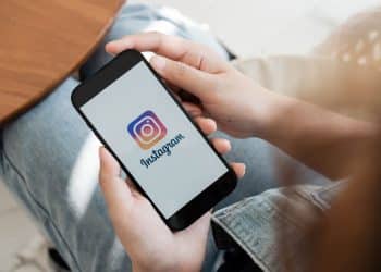 Mãos segurando smartphone preto com logo do Instagram.