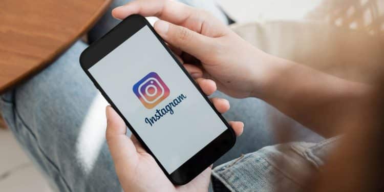 Mãos segurando smartphone preto com logo do Instagram.