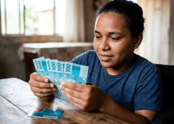 Mulher cadeirante conta notas de R$ 100 em ambiente doméstico.