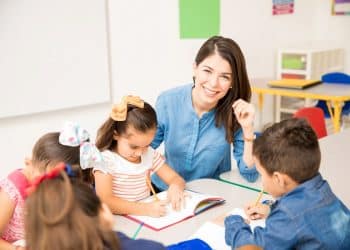 Professora sorridente acompanha crianças em atividade escolar.