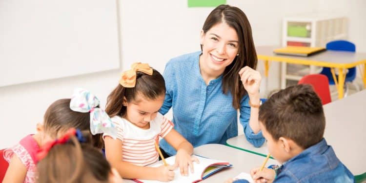 Professora sorridente acompanha crianças em atividade escolar.