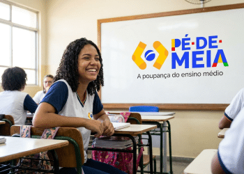 Estudante sorrindo em sala de aula com logo do programa Pé-de-Meia.