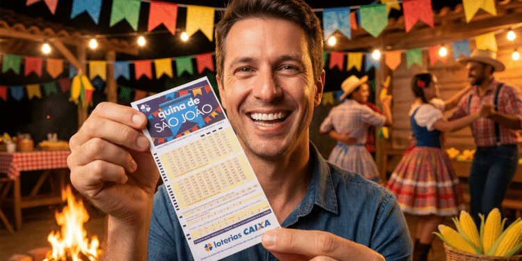Homem sorridente exibe volante da Quina de São João com bandeirinhas e fogueira de festa junina ao fundo.