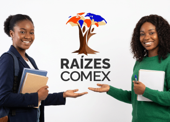 Duas jovens negras sorrindo e apontando para logo do Raízes Comex, uma com blazer e livros, outra com blusa verde e caderno.