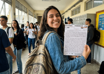 Estudante exibe folha de redação do ENEM em corredor de escola.