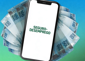 Smartphone exibindo texto "Seguro-Desemprego" sobre notas de 100 reais dispostas em leque.