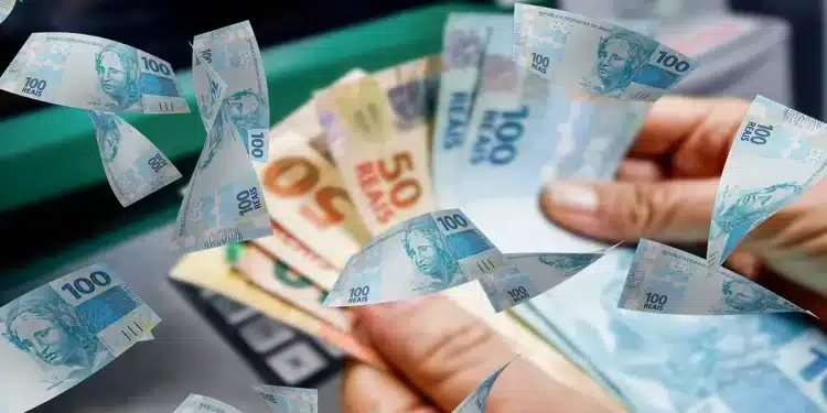 Notas de real sendo seguradas com outras cédulas de dinheiro ao fundo, representando o pagamento do Abono Salarial PIS/Pasep 2026 e a variação dos valores recebidos pelos trabalhadores.
